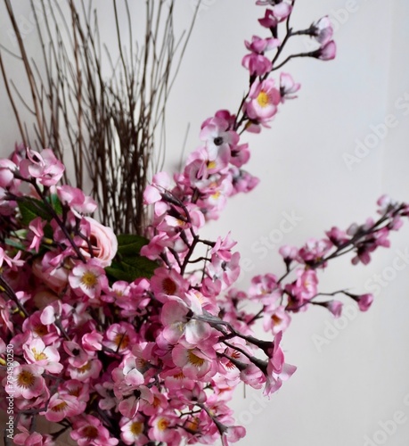 Pink flower sakura cherry blossom petals plastic indoor decorative syntethic flora isolated on plain wall background. photo