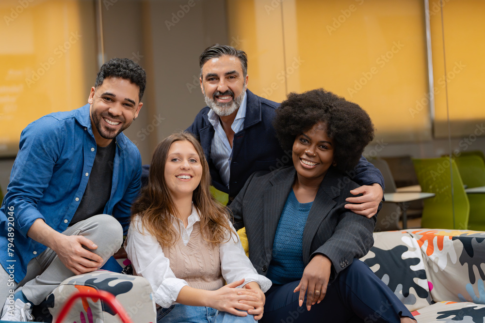 Diverse team of happy colleagues posing together on a colorful patterned sofa in a creative office space. 