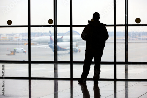 Passenger in the airport, silhouette of man looking at the planes on the tarmac through the glass