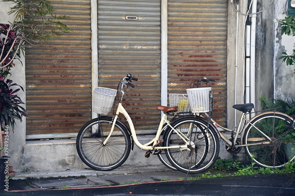 This photo depicts a daytime scene in an alley with two parked bicycles. The house behind them is closed, creating a tranquil atmosphere and highlighting the charm of traditional Taiwanese alleys.