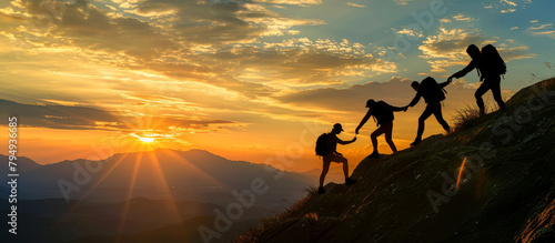 Silhouetted group of hikers helping each other climb a mountain at sunset