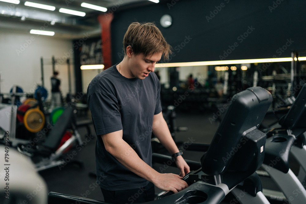 Portrait of athletic man in activewear adjusting settings on treadmill, preparing for cardio session in well-equipped gym. Sporty male walking on running track, working on health and fitness. Portrait of athletic man in activewear adjusting settings on treadmill, preparing for cardio session in well-equipped gym. Sporty male walking on running track, working on health and fitness.