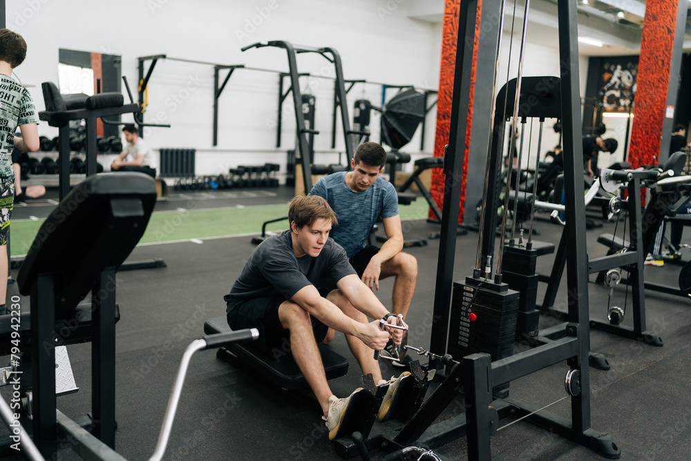Remote wide shot of beginner sportsman with personal instructor working out in gym by using rowing machine. Sweating man doing exercises for back muscles under supervision of trainer measuring time Remote wide shot of beginner sportsman with personal instructor working out in gym by using rowing machine. Sweating man doing exercises for back muscles under supervision of trainer measuring time