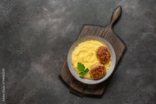 Mashed potatoes with meat cutlet in a bowl on a wooden board, dark grunge background. Top view, flat lay, copy space.