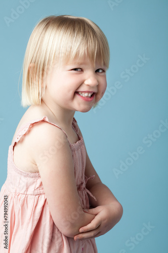 Little girl, smile and playful in studio with portrait for child development on blue background. Sneaky, rascal and confident in childhood with youth for joy with fun, happy and innocent cute face
