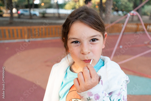 A young girl pauses for a reflective moment with her lollipop, creating a portrait of childhood contemplation