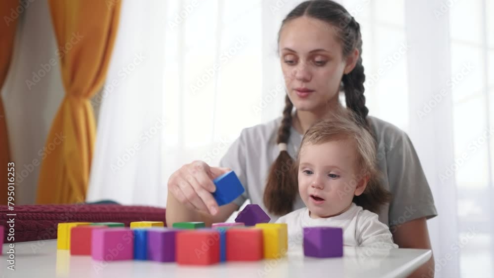 mother plays with her child. happy childhood dream concept for a little child. a small child sits at the white table on his mother lap and lifestyle plays with beautiful colorful cubes mother plays with her child. happy childhood dream concept for a little child. a small child sits at the white table on his mother lap and lifestyle plays with beautiful colorful cubes