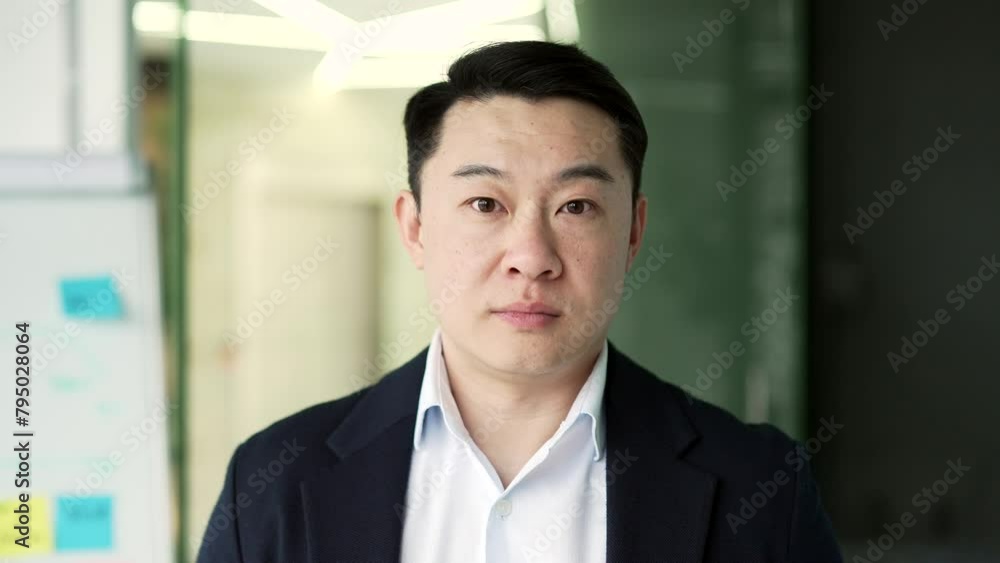 Portrait of a serious asian businessman standing at workplace in business office. Confident mature man in a formal suit posing looking at camera. Head shot of a successful entrepreneur. Close up Portrait of a serious asian businessman standing at workplace in business office. Confident mature man in a formal suit posing looking at camera. Head shot of a successful entrepreneur. Close up