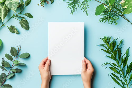 Hands holding white paper blank on blue background with green leaves