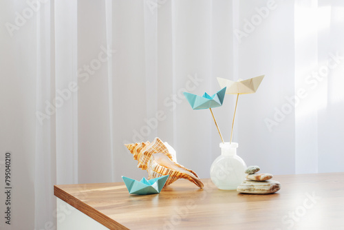 paper boats in glass vase with sea decor on wooden table