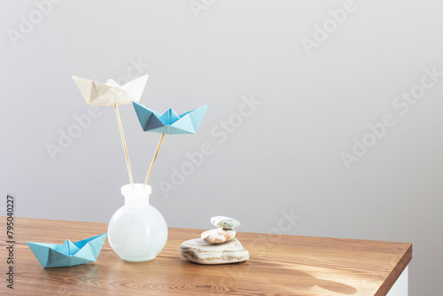 paper boats in glass vase with sea stones  on wooden table