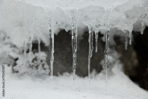visuale in primo piano e di fronte di varie stalattiti di ghiaccio in un ambiente naturale di montagna, che si sono formate dallo scioglimento della neve sovrastante photo