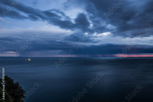 inquadratura panoramica dall'alto, vicino a Sistiana che mostra un temporale lontano che si abbatte sul Golfo di Trieste, nel Mare Adriatico, di sera, al tramonto, con un cielo completamente nuvoloso, photo