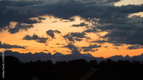 visuale in primo piano di un cielo nuvoloso durante un tramonto color arancione e delle sagome scure delle montagne distanti viste da lontano  photo