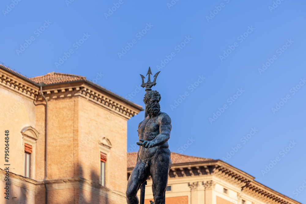 Naklejka premium The imposing Neptune statue dominates the scene at Bologna Fountain of Neptune, crowned with a regal trident against a backdrop of clear blue sky and historic architecture
