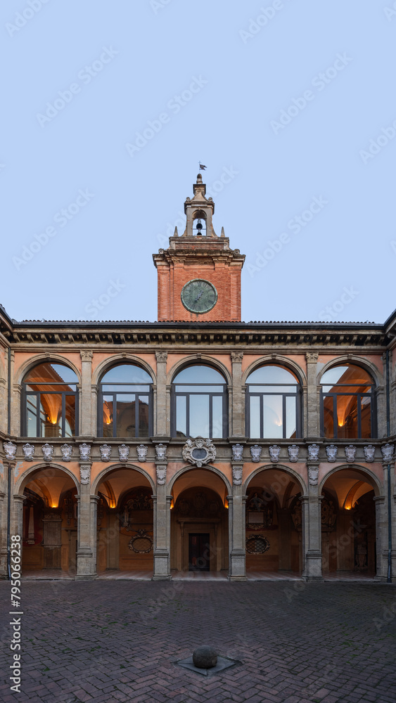 Dusk descends on the inner courtyard of the University of Bologna, with the clock tower standing as a historic beacon against the twilight sky