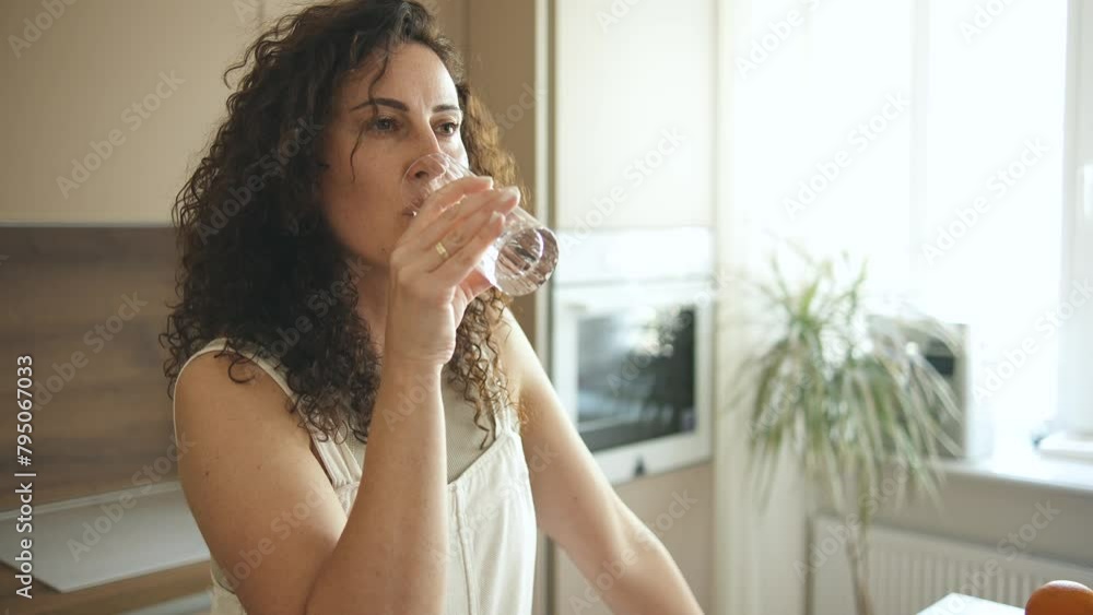 Smiling curly woman in domestic kitchen drinking clean mineral still water Smiling curly woman in domestic kitchen drinking clean mineral still water