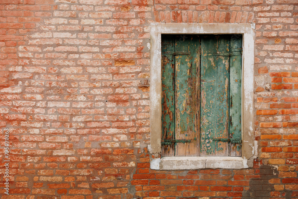 The facade of a typical exposed brick house with window and green shutters in Venice, Italy