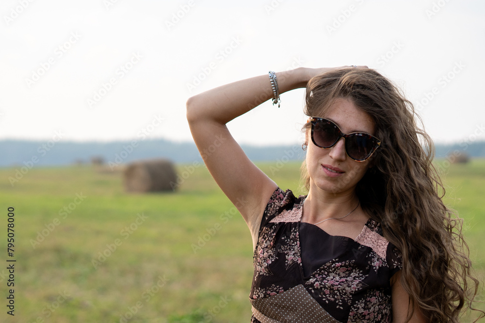 a beautiful girl with curly hair rests on a field next to a haystack on a warm and sunny summer day
a beautiful girl with curly hair rests on a field next to a haystack on a warm and sunny summer day