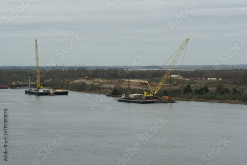 Heavy machinery crane on floating barge  near the left bank of the Savannah River loading sand and clay from shore as building material for construction of new terminal. 
