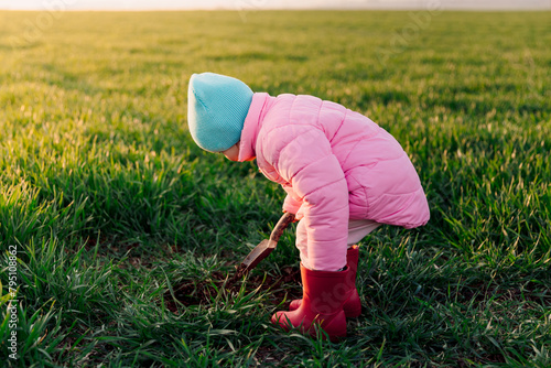 Portrait of kid girl in the field digging the ground with a shovel