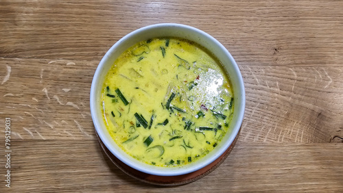 A bowl of curry coconut soup on a table made of wood, with fine herbs as ingredients Hanover Germany