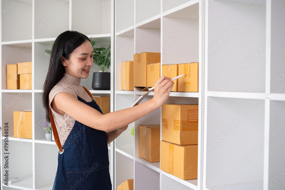A small SME business owner receives product orders and writes shipping information on cardboard boxes in the home office to prepare for delivery. A small SME business owner receives product orders and writes shipping information on cardboard boxes in the home office to prepare for delivery.
