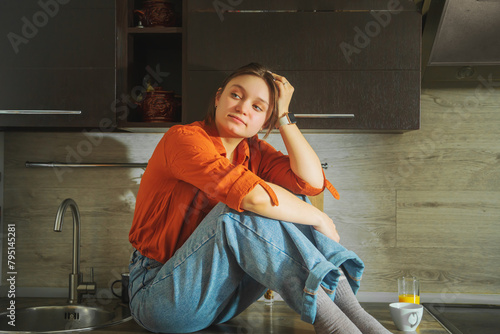 Beautiful young woman sitting on the kitchen countertop.