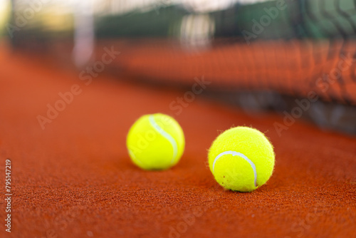 tennis balls on orange clay court with blurred net in background © angyim
