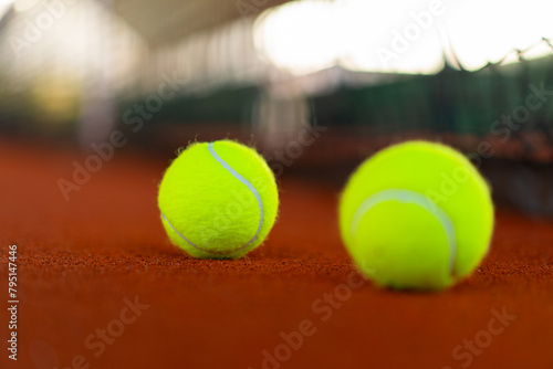 tennis balls on orange clay court with blurred net in background © angyim