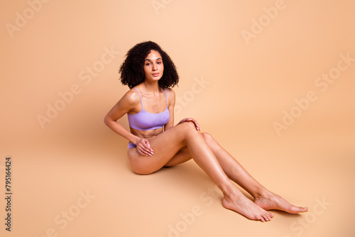 Full body no filter portrait of stunning model girl sit floor touch leg isolated on beige color background