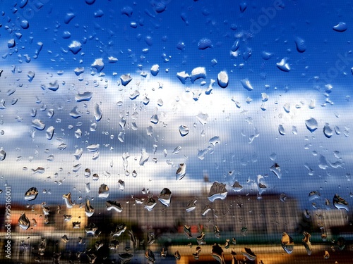 Water drops on glass with blue sky and white clouds as background. © kos1976