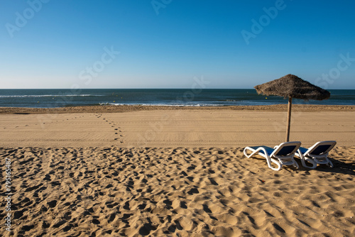 Beautiful summer landscape of the Spanish coast, two sun loungers, sun loungers and parasol. Fine golden sand, sea view with horizon,blue sky, calm and relaxation. Inspiring vacation landscape.