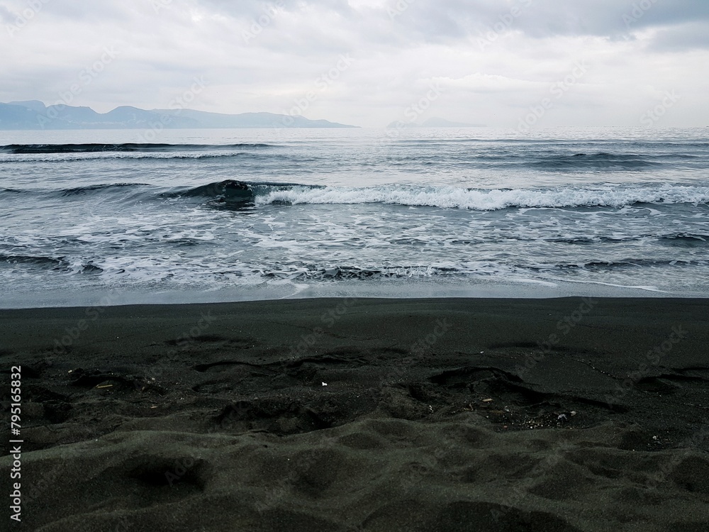 Black sand beach with waves crashing on it and mountains in the background Black sand beach with waves crashing on it and mountains in the background