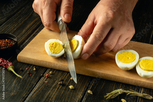 Close-up of a man hands with a knife slicing a boiled egg on a kitchen cutting board before preparing a breakfast dish at home