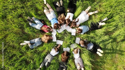 Girls students lie on the grass in a city park with notebooks.