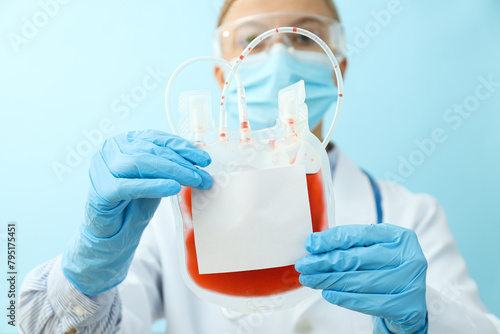 Doctor with bag with donor blood in hands on blue background, close up