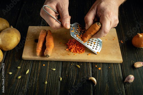 Close-up of a chef hands grating carrots on a kitchen board before preparing a vegetarian breakfast dish.
