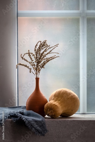 Still life with a pumpkin and a dry branch in a vase on the windowsill