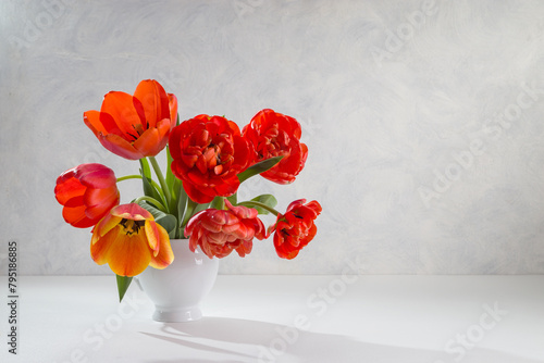 A bouquet of red tulips in a white vase on a light background. Copy space