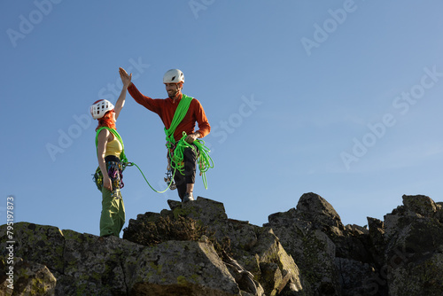Two people are standing on a rocky mountain top, one of them giving the other a high five. Concept of accomplishment and camaraderie, as the two climbers have reached the summit together