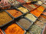 A variety of spices are displayed in different colored containers. The spices include cumin, paprika, and turmeric