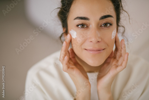 Young woman 30 years old applying face cream on her skin.