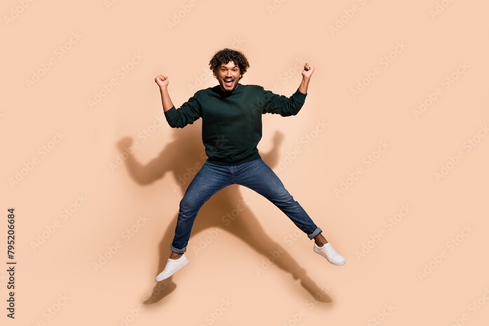 Full body portrait of nice young man jump raise fists wear sweater isolated on beige color background
