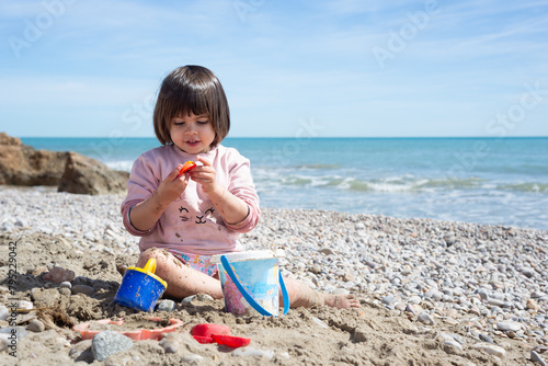 Smiling little girl playing with toys on a mediterranean sandy beach at a sunny spring day.