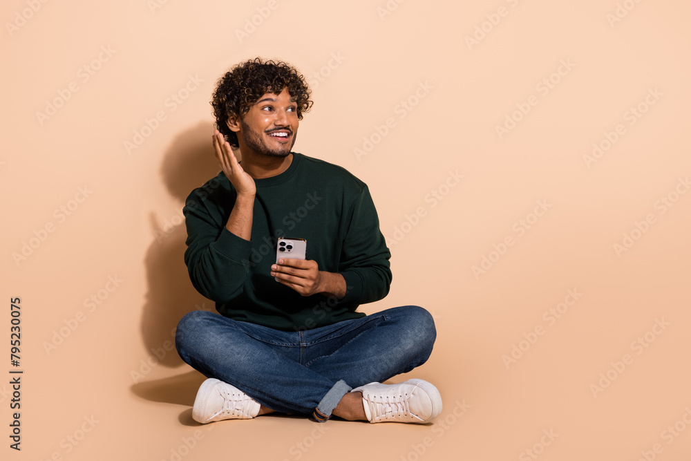Full body portrait of nice young man hold phone empty space wear sweater isolated on beige color background Full body portrait of nice young man hold phone empty space wear sweater isolated on beige color background