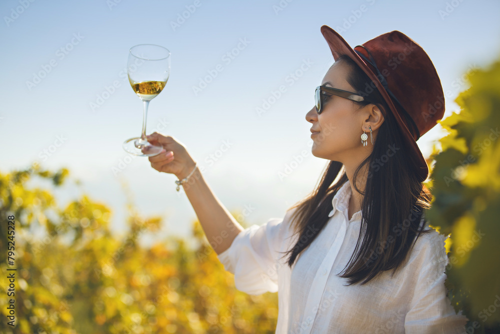 Obraz premium Woman Tasting White Wine in Glass on Plantation of Vineyard