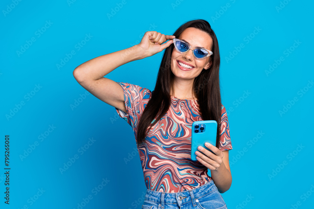 Fototapeta premium Photo portrait of pretty young girl touch sunglass hold device wear trendy colorful clothes isolated on blue color background