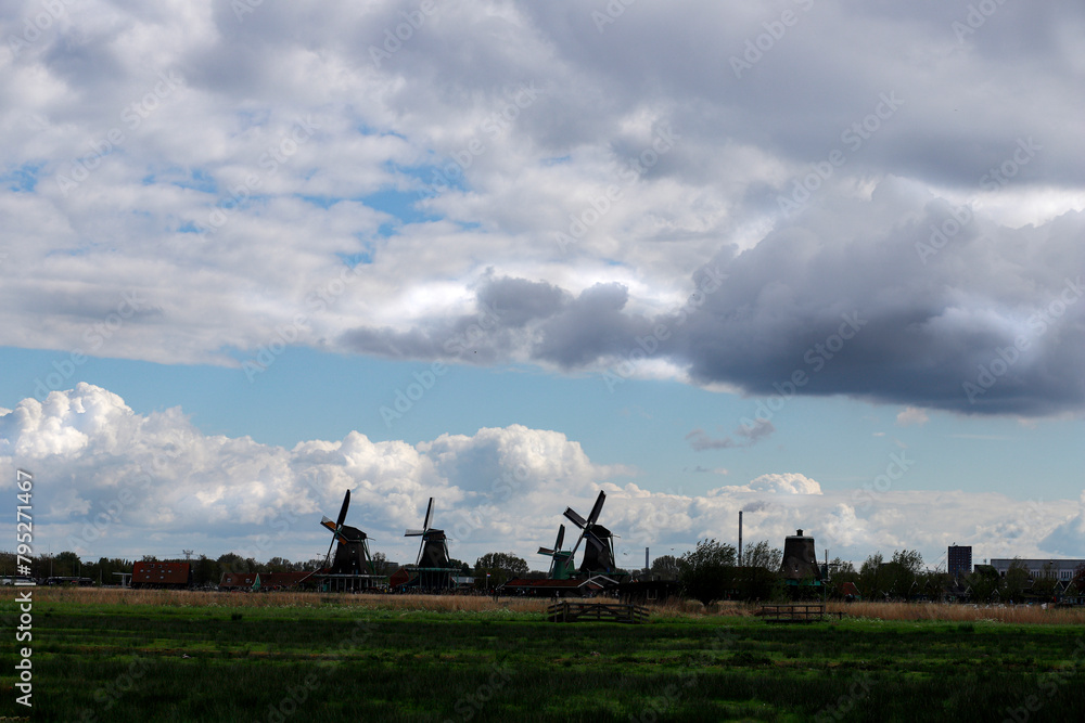 Naklejka premium Meadow in the foreground and windmills in the background, very cloudy sky in the Zaanse Schans area in Netherlands.