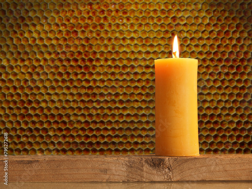 Burning candle made of beeswax in front of a honeycomb background with space for text